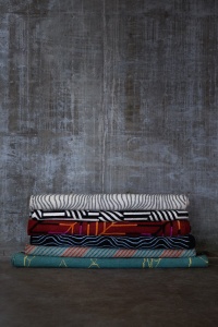 Colorful design rugs piled against a concrete wall